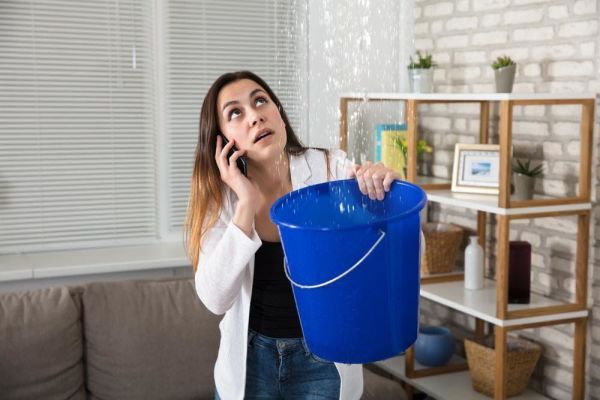 Woman on the phone holding a bucket up to a cieling leak