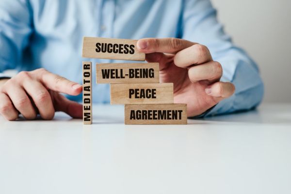 Wood blocks labeled: success, well-being, peace, agreement, and mediation stacked up