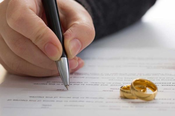 Person signing paper. Two wedding rings rest on the paper